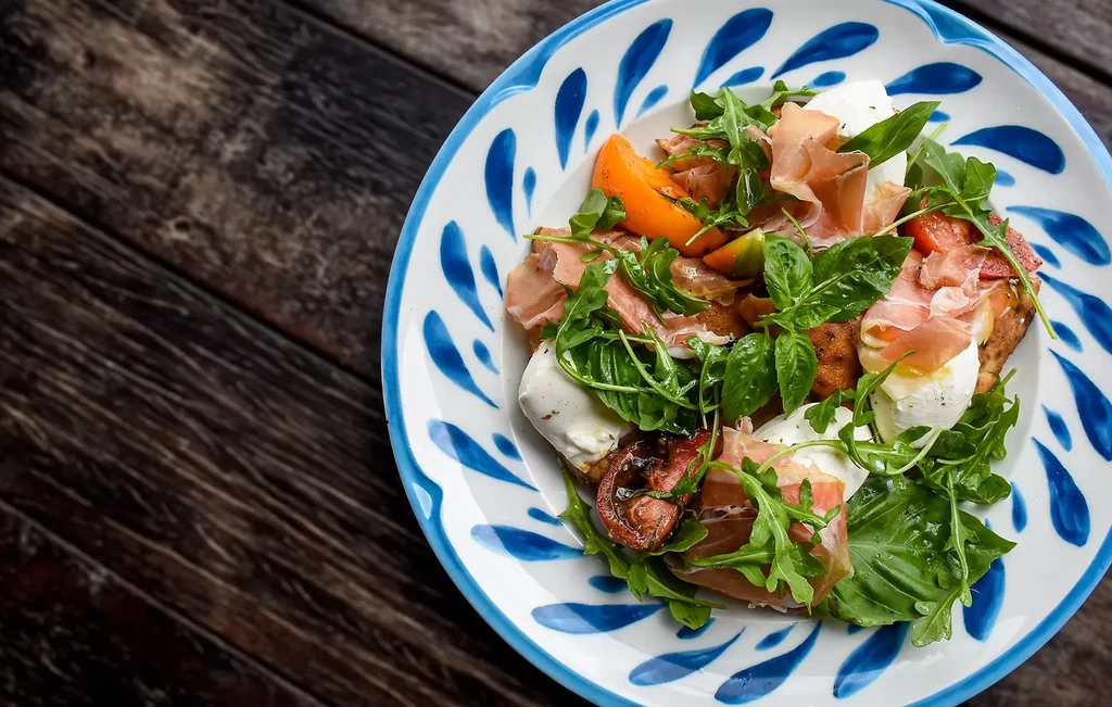 Bruschetta with prosciutto, mozzarella, tomatoes, arugula on a rustic table.