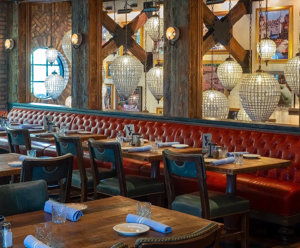 Restaurant dining room with red banquette, rustic wood, and crystal chandeliers.
