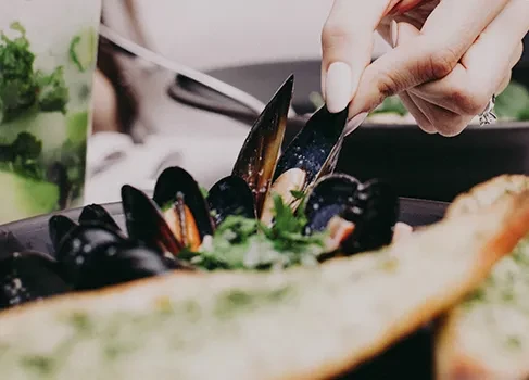 Close-up: hand picking a mussel from a plate with herbs.
