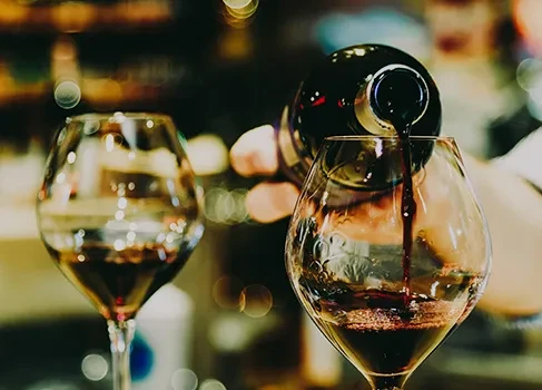 Red wine pours from bottle into stemmed glass; another visible.