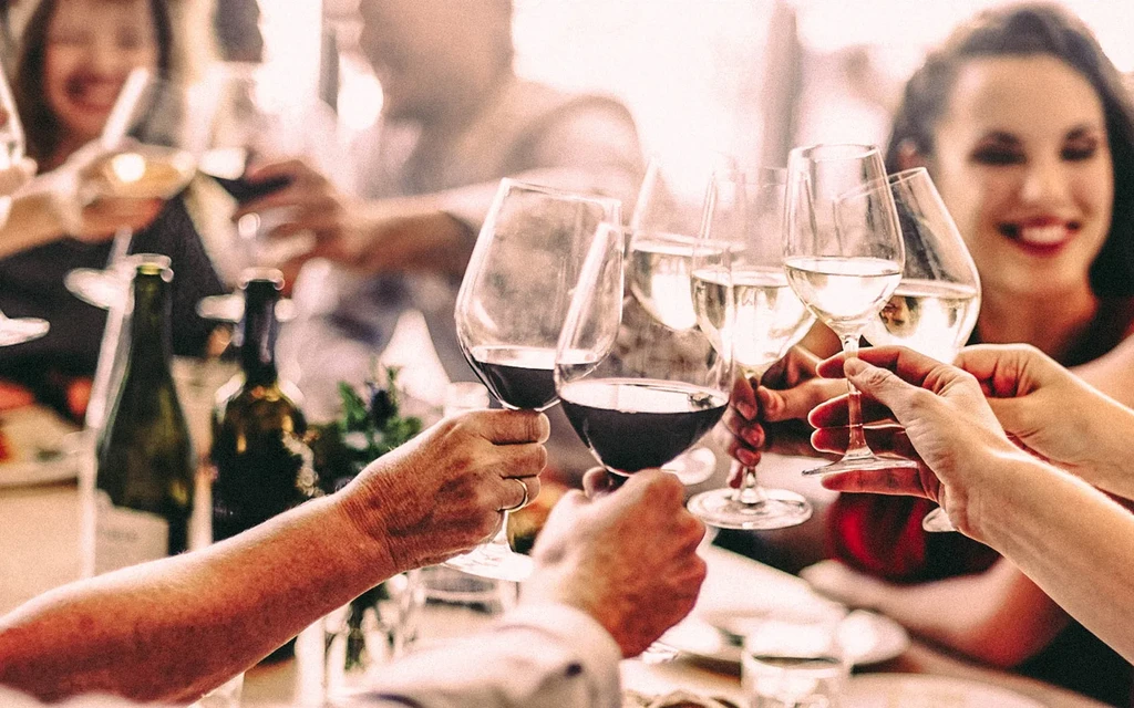 Multiple hands clinking red and white wine glasses in a toast.