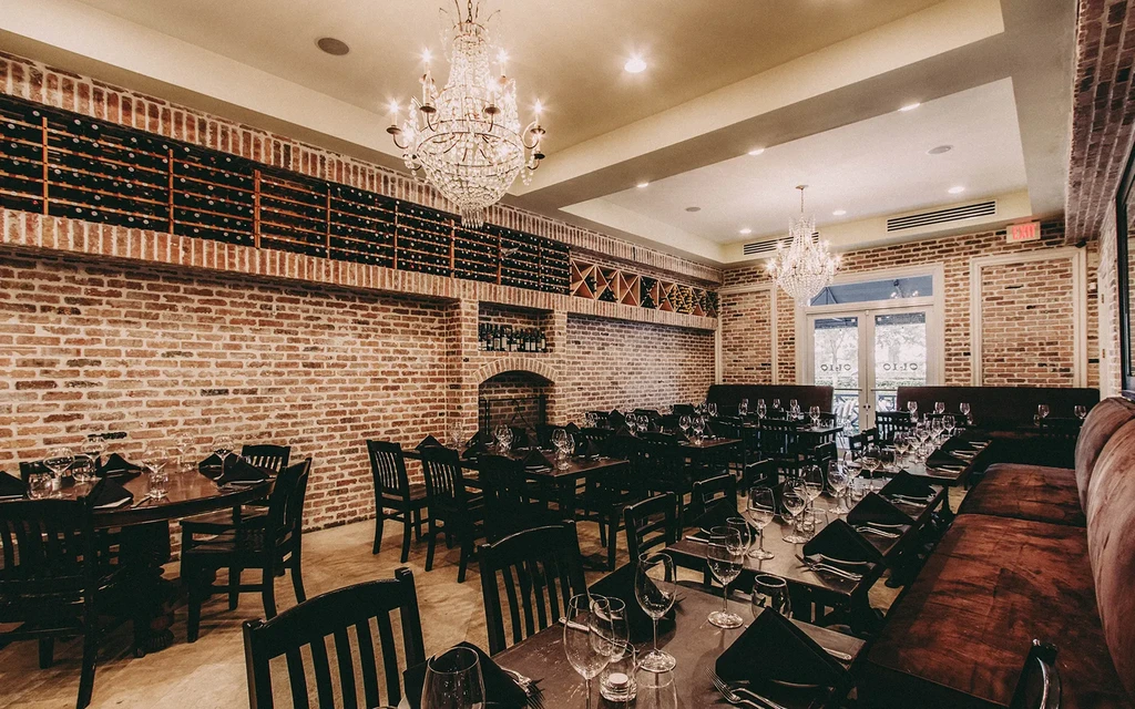 Rustic-chic restaurant interior with exposed brick, wine shelves, and chandeliers.