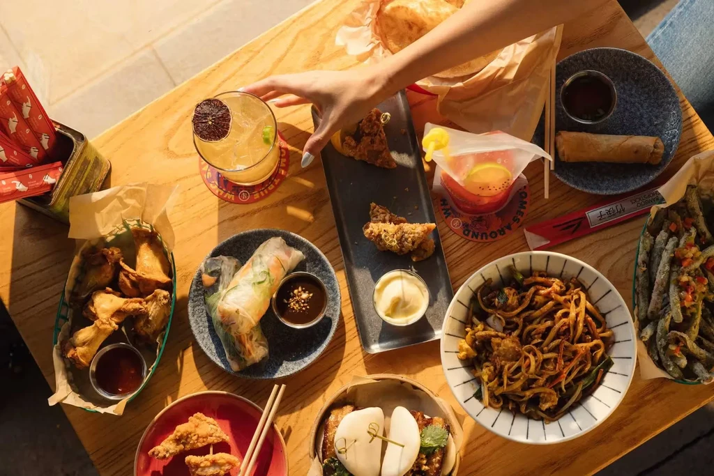 Overhead view of Asian food and cocktails on a table in sunlight.