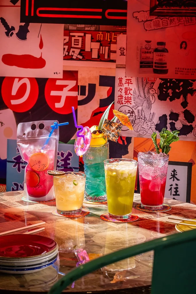 Five vibrant cocktails on reflective table, with Asian posters and neon.