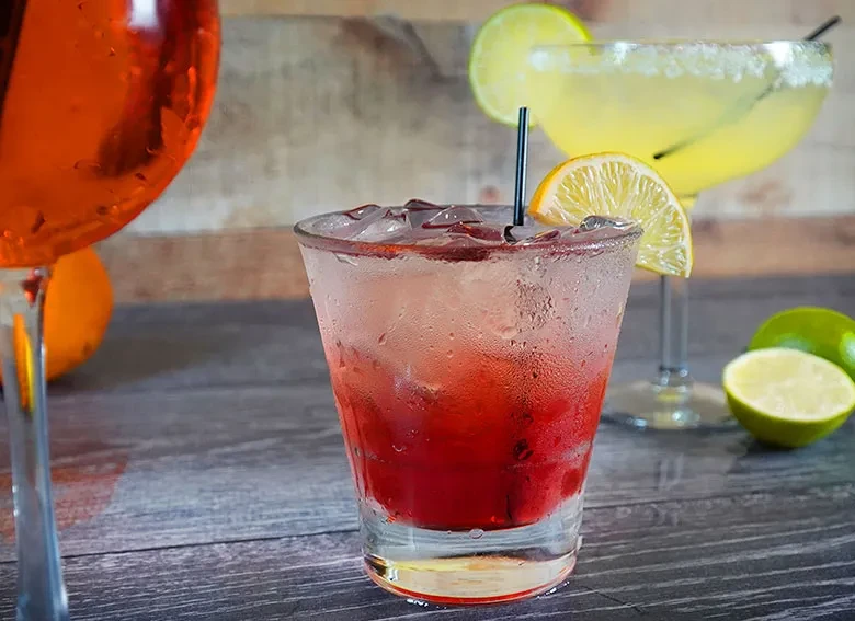 Three vibrant cocktails with fruit garnishes on a rustic wooden surface.
