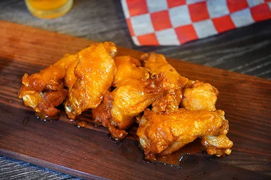 Crispy, saucy buffalo chicken wings on a wooden board.