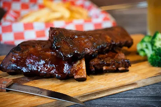Barbecue ribs with dark glossy sauce on a wooden board and knife.