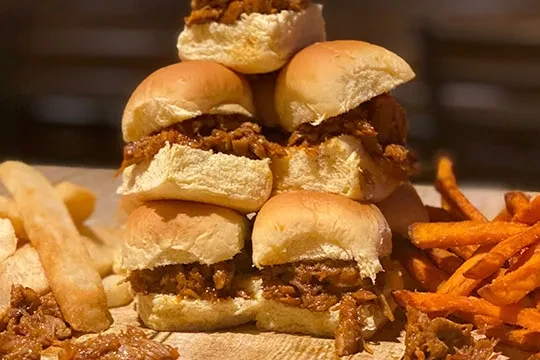 Stacked meat sliders with thick-cut and sweet potato fries on wood.