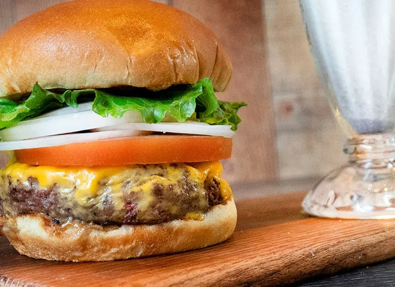 Fresh cheeseburger with melted cheese, lettuce, and tomato on a wooden board.