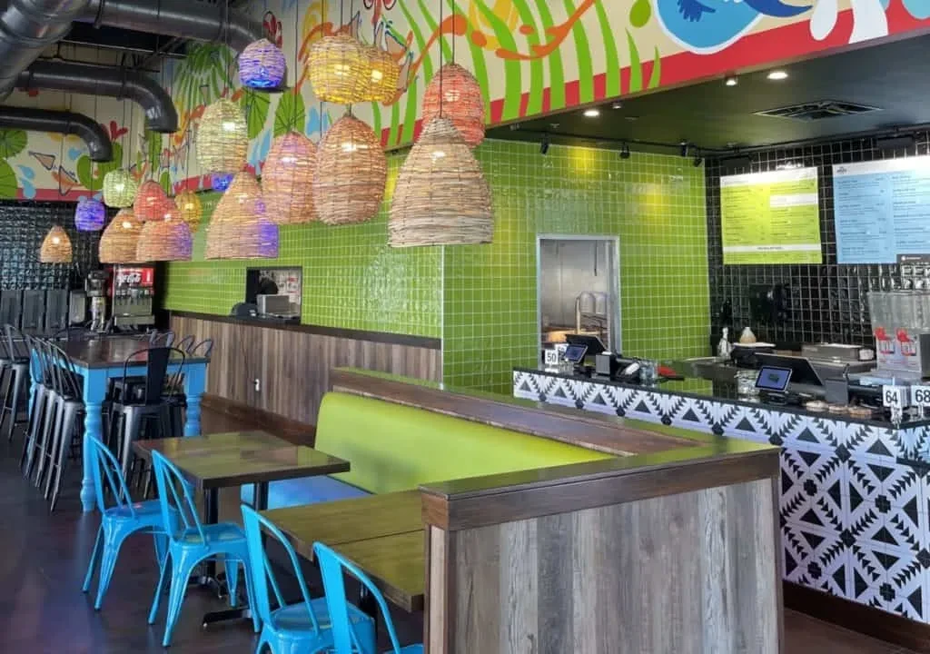 Modern restaurant interior with colorful pendant lights, abstract mural, and diverse seating.