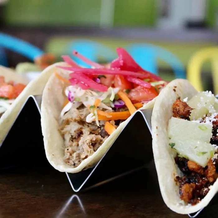 Three tacos with meat, colorful slaw, pineapple in a holder.