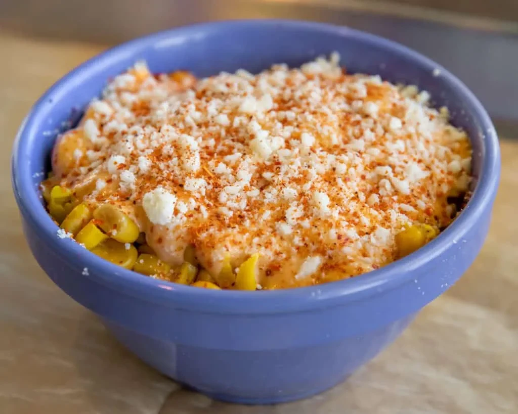 Periwinkle bowl of corn with creamy orange sauce, cotija cheese, chili.