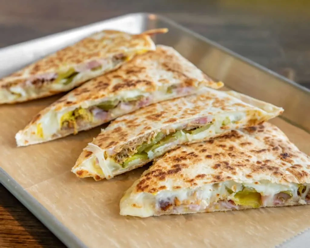 Four toasted quesadilla slices with melted cheese, ham, and pickles.
