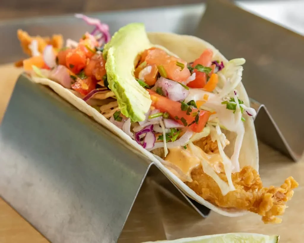 Seafood taco with avocado, cabbage, and sauce in a metal holder.