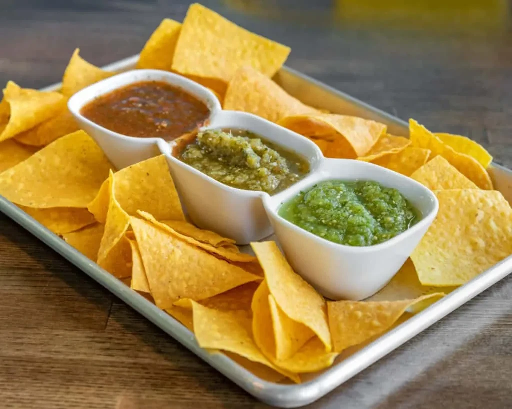 Tray of golden tortilla chips with three different chunky salsas.