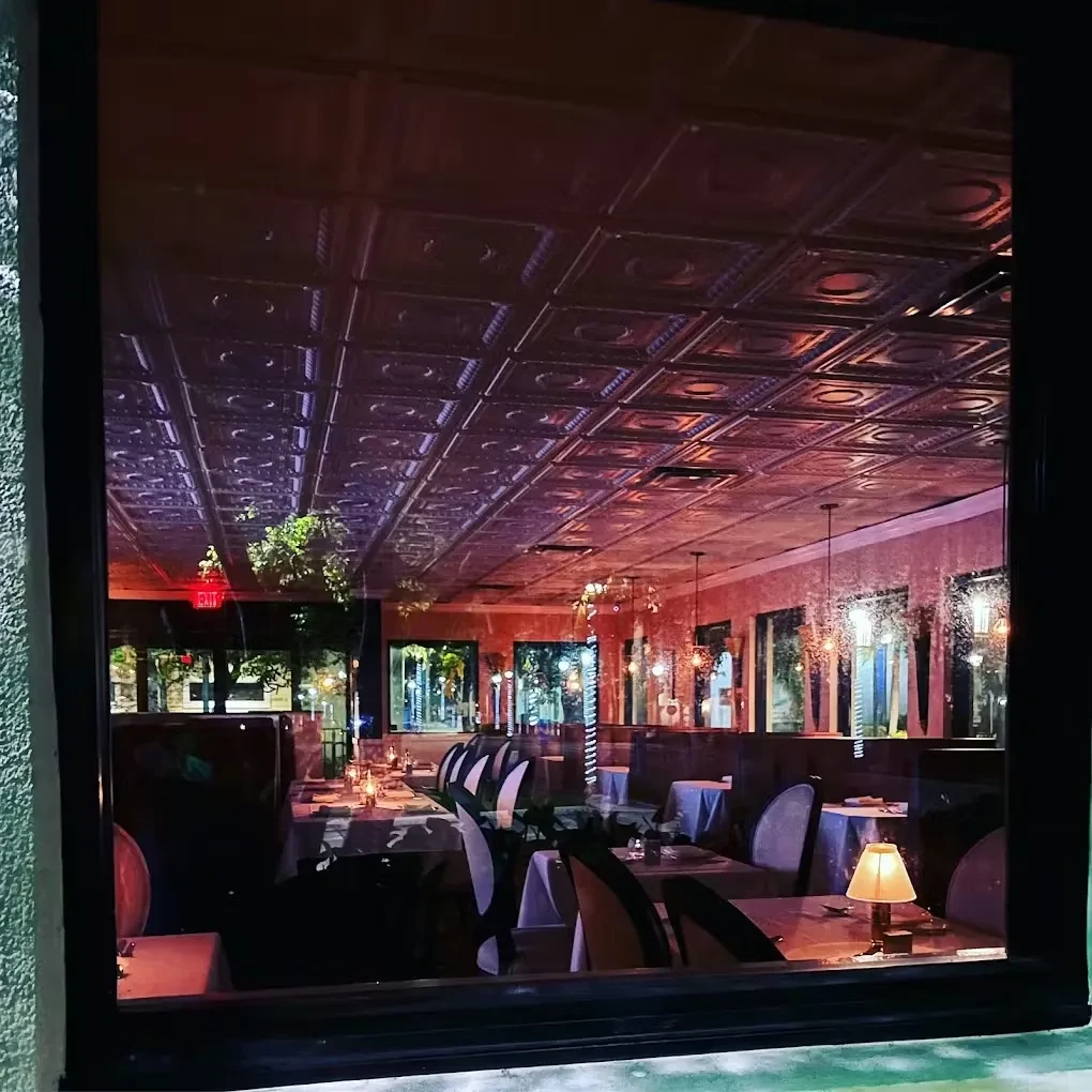 Empty restaurant interior at night; warm lighting, decorative ceiling, set tables.