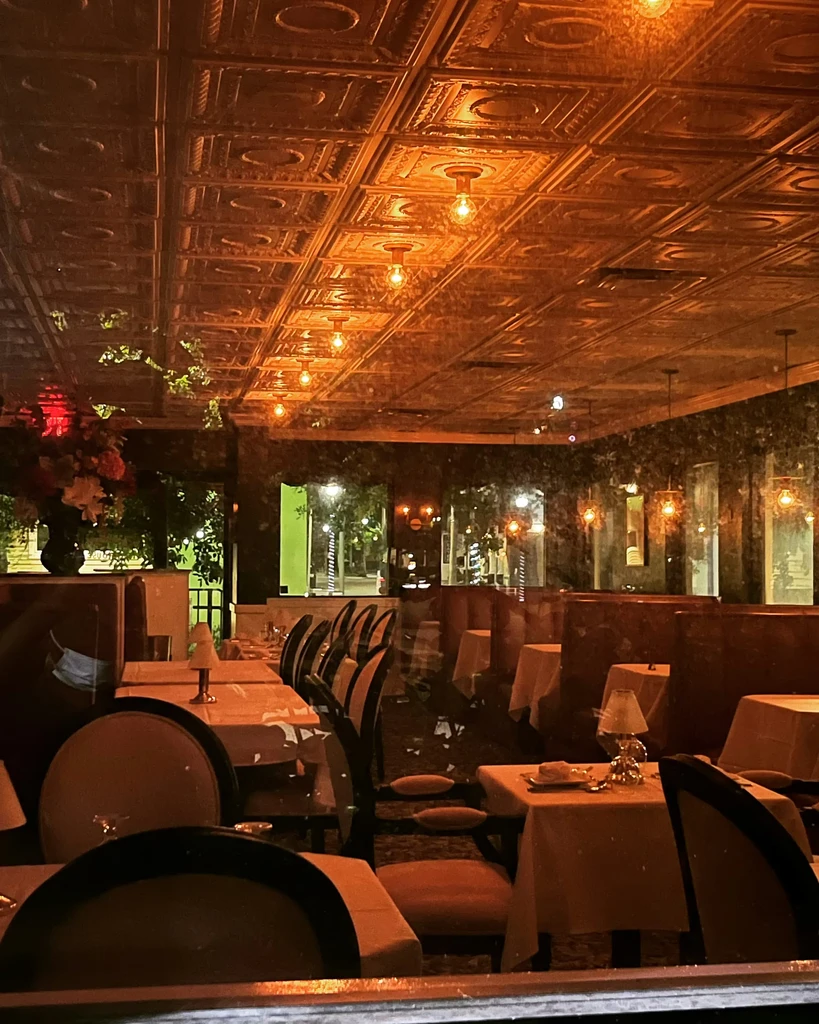 Upscale restaurant dining room with ornate tin ceiling and warm amber light.