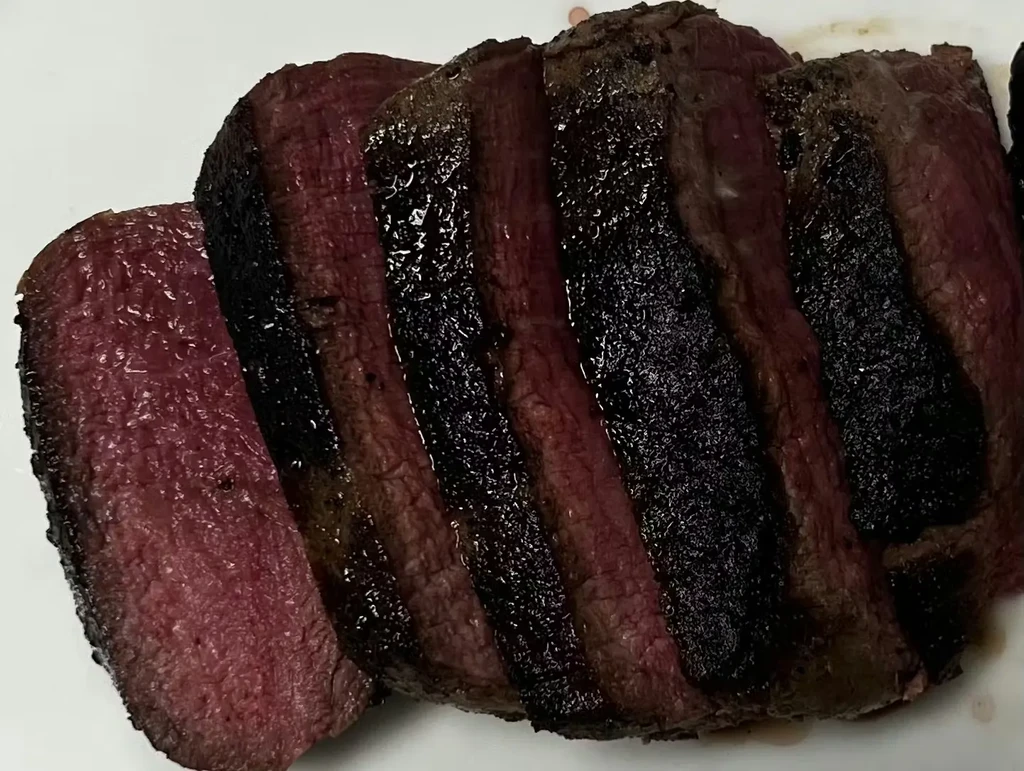 Sliced medium-rare steak, dark charred exterior, glistening red interior.