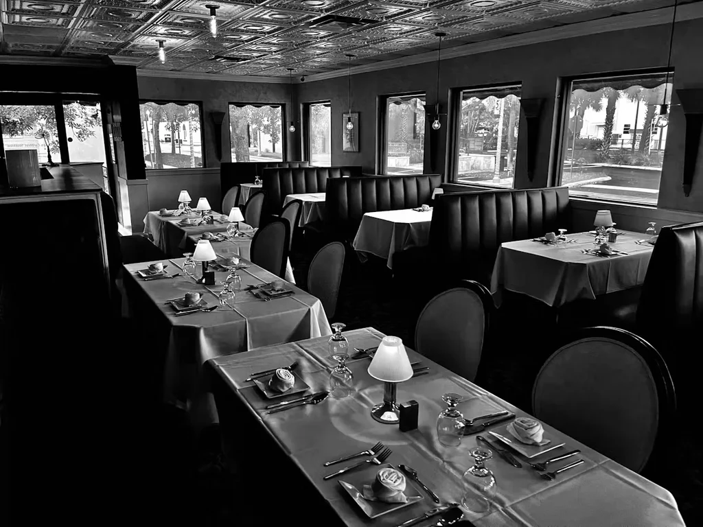 Black and white photo of an empty restaurant with many set tables.