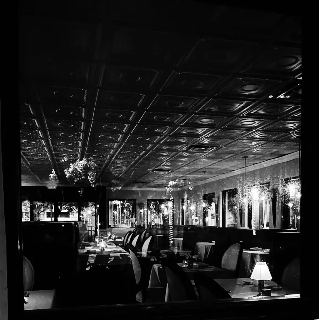 Black and white restaurant interior with ornate ceiling and warm table lamp.