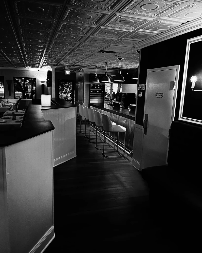 Black and white bar interior with modern stools and ornate tin ceiling.
