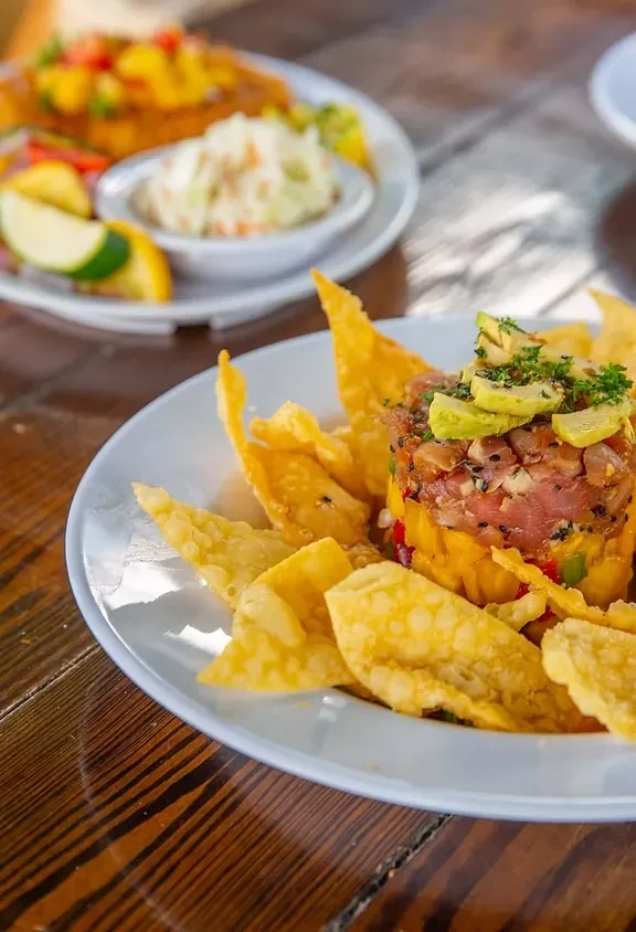 Vibrant tuna tartare stack with chips and blurred fish dish.