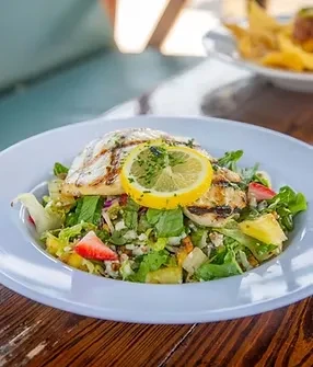 Grilled fish fillet on a vibrant salad with fruit, lemon, and herbs.