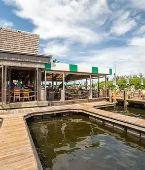 Rustic waterfront restaurant with open doors and striped awning.