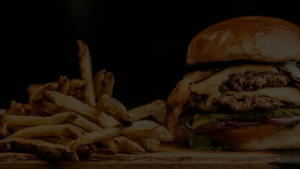 Close-up of a double cheeseburger and fries in low-key lighting.