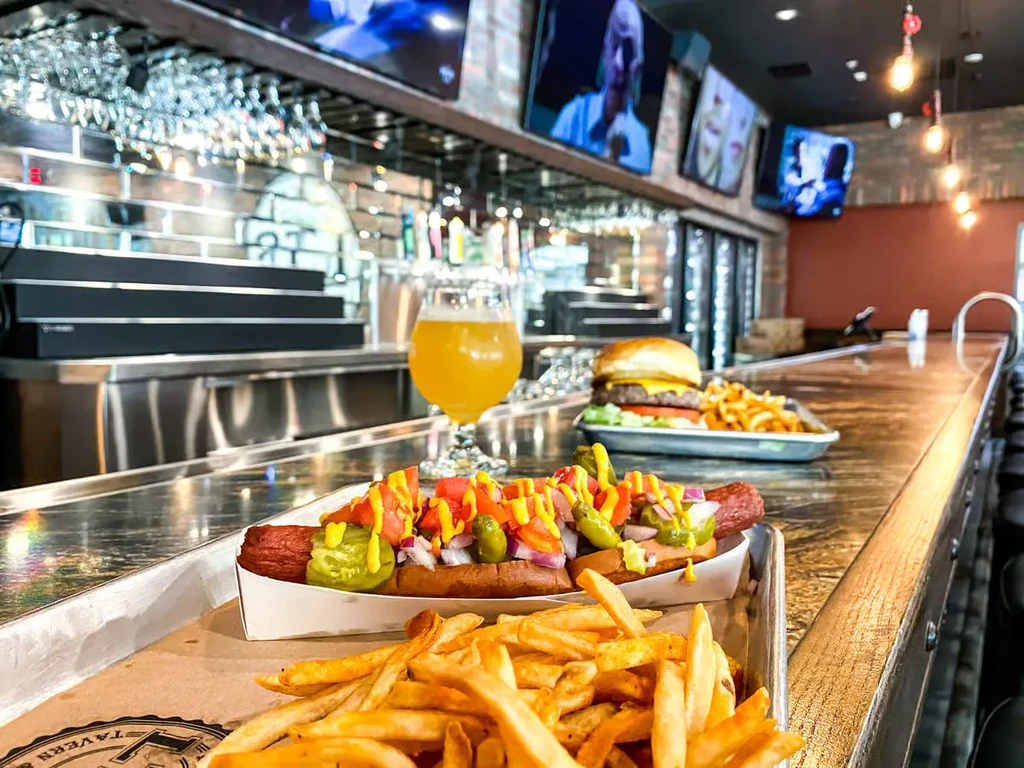 Loaded hot dog, fries, and beer on a wooden bar.