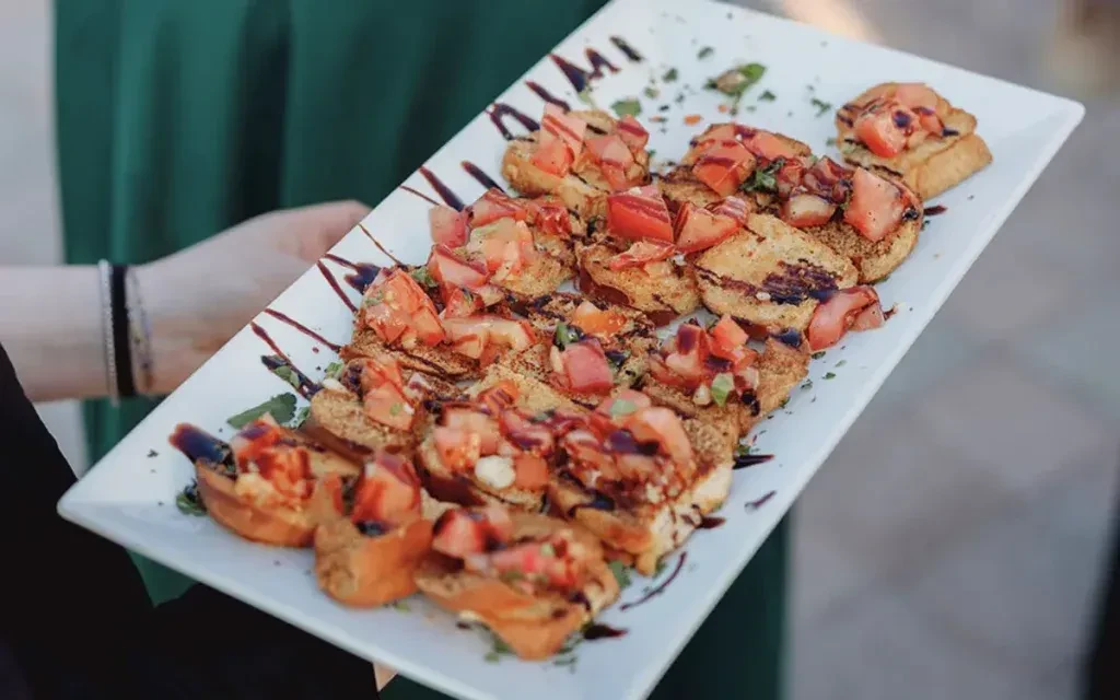 White plate with bruschetta topped with tomatoes, herbs, and balsamic glaze.