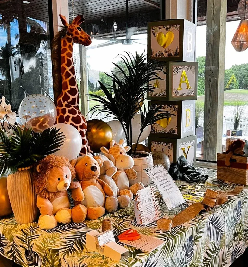 Jungle baby shower table with stuffed animals, balloons, and 'BABY' blocks.