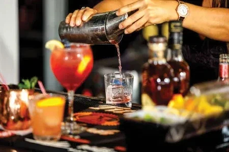 Bartender's hands pour drink from shaker into ice-filled glass; other drinks.