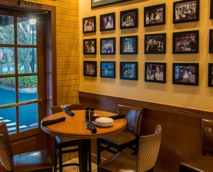 Restaurant interior showing a set table, window view, and framed photo gallery.
