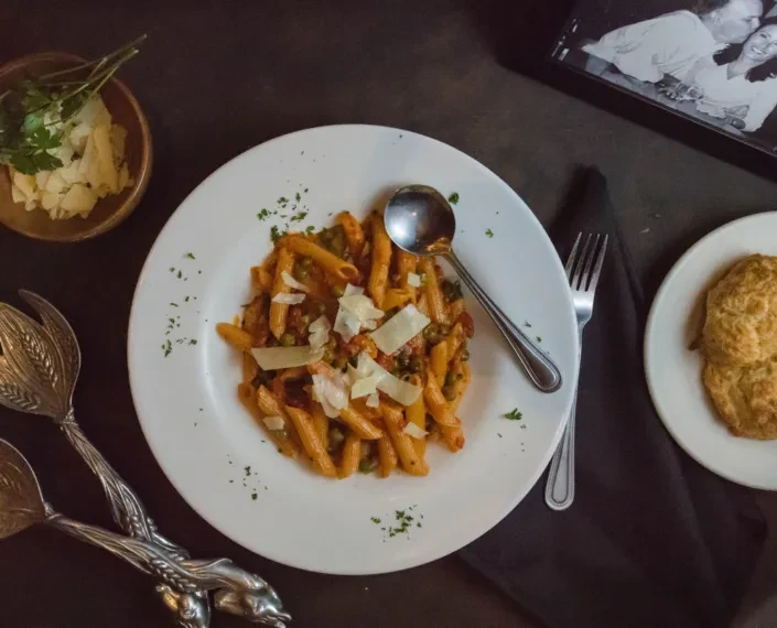 Penne pasta with peas, Parmesan, rolls, serving tongs, and a framed photo.