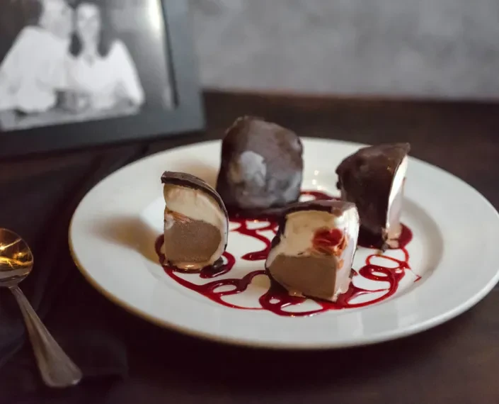 Four chocolate-covered layered frozen desserts with red sauce.