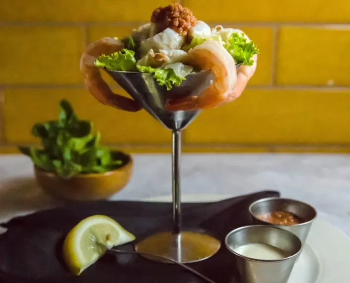 Shrimp cocktail in martini glass, shrimp over rim, lemon and sauces.