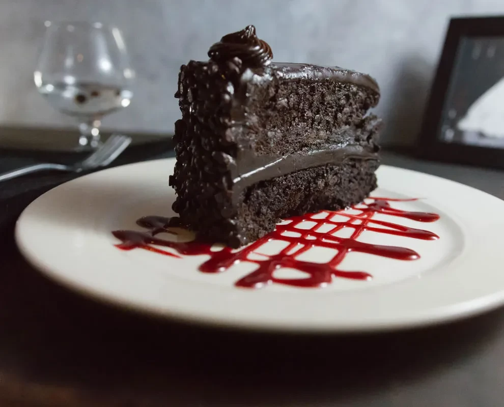 Single slice of layered dark chocolate cake on plate with red sauce.