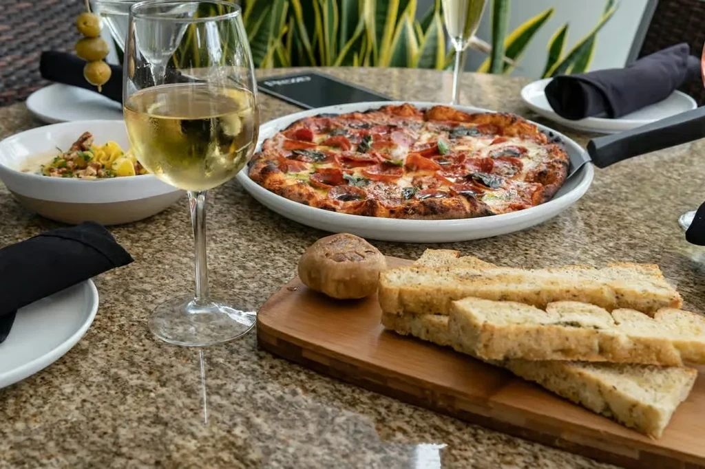 Pepperoni pizza, pasta, garlic bread, and white wine on an outdoor table.