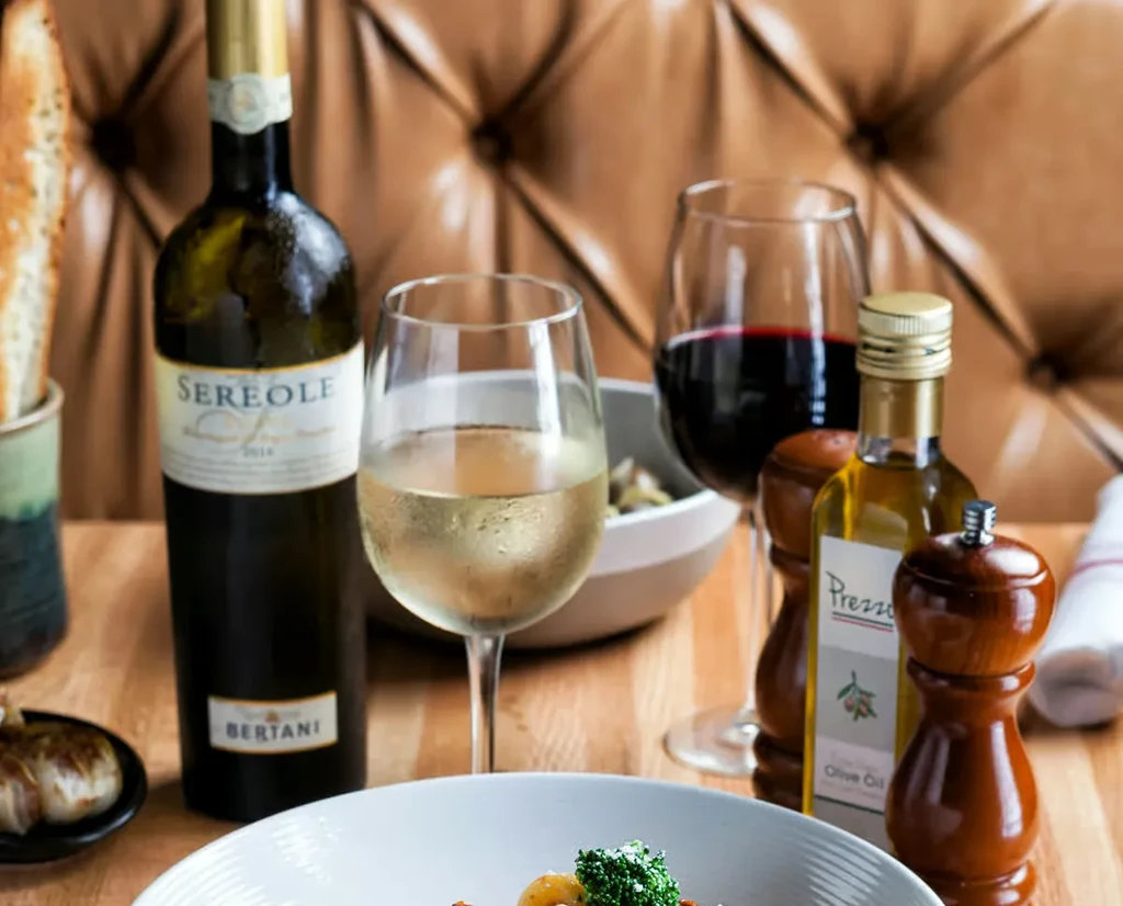 Restaurant table with white wine, food, olive oil, and pepper grinder.