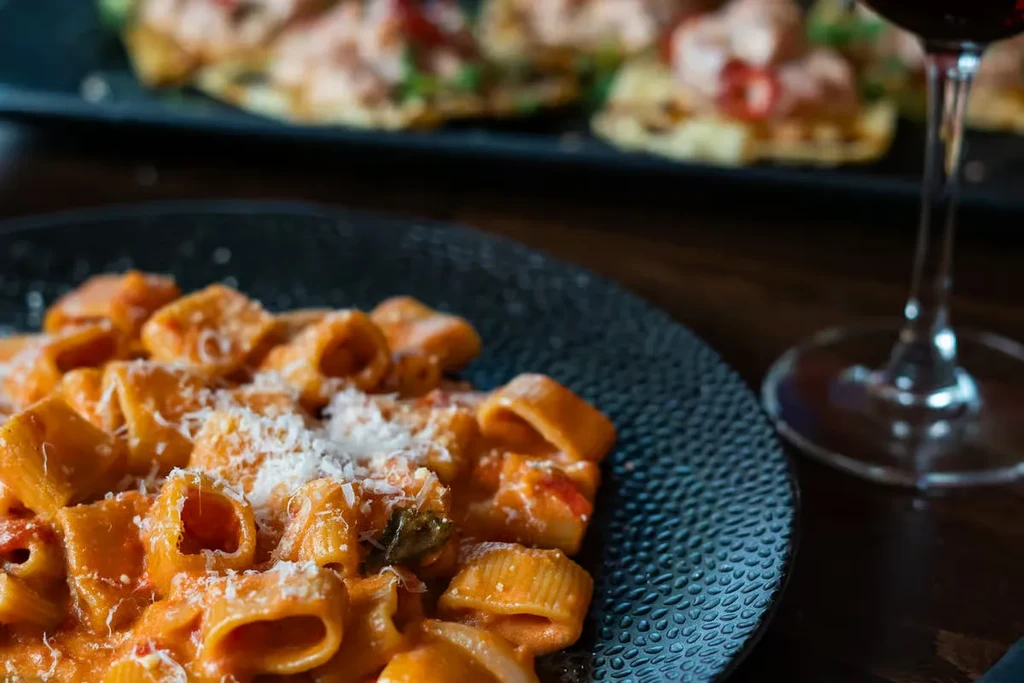 Plate of rigatoni pasta with orange-red sauce and white cheese.