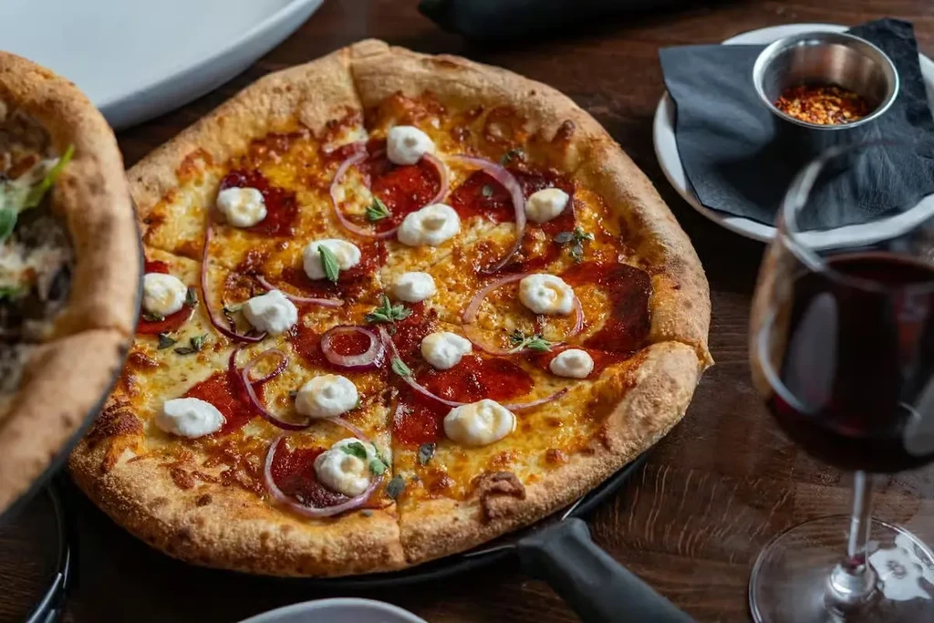 Freshly baked pizza with pepperoni, cheese, ricotta, onion, on wood.