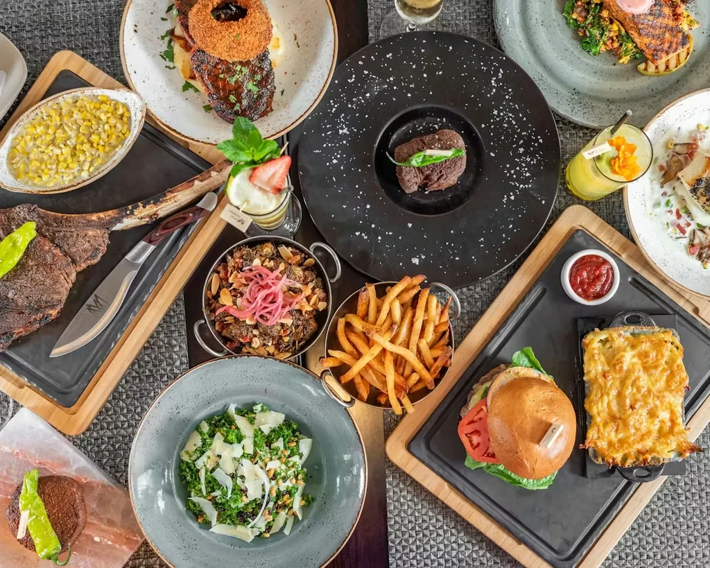 Overhead shot of a table with steaks, burger, mac and cheese, drinks.