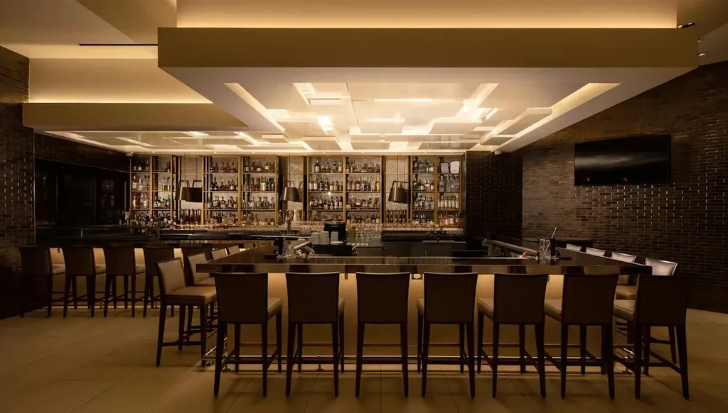 Sophisticated bar interior with well-stocked shelves, warm lighting, and empty stools.