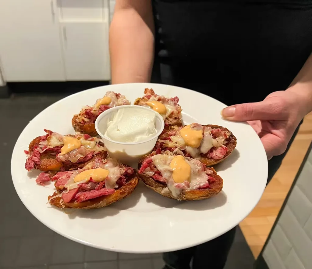Hand holds plate of five corned beef appetizers with cheese and dip.