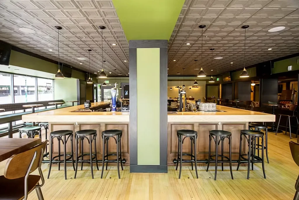 Modern restaurant with U-shaped bar, green pillar, and pressed tin ceiling.