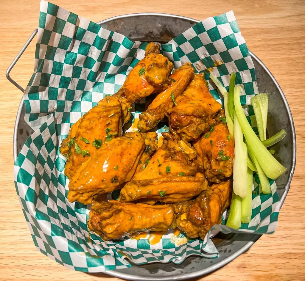 Saucy chicken wings, celery, and herbs in a galvanized bucket.