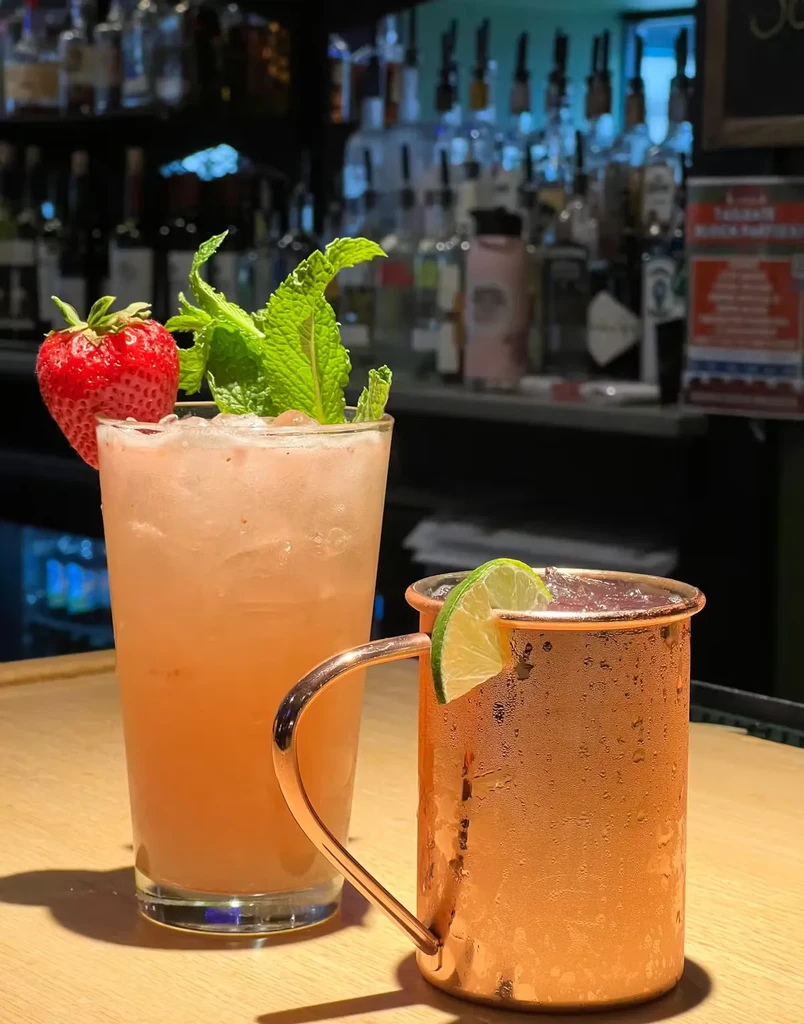 Two garnished cocktails: a pink drink with strawberry and mint, and a copper mug with lime.