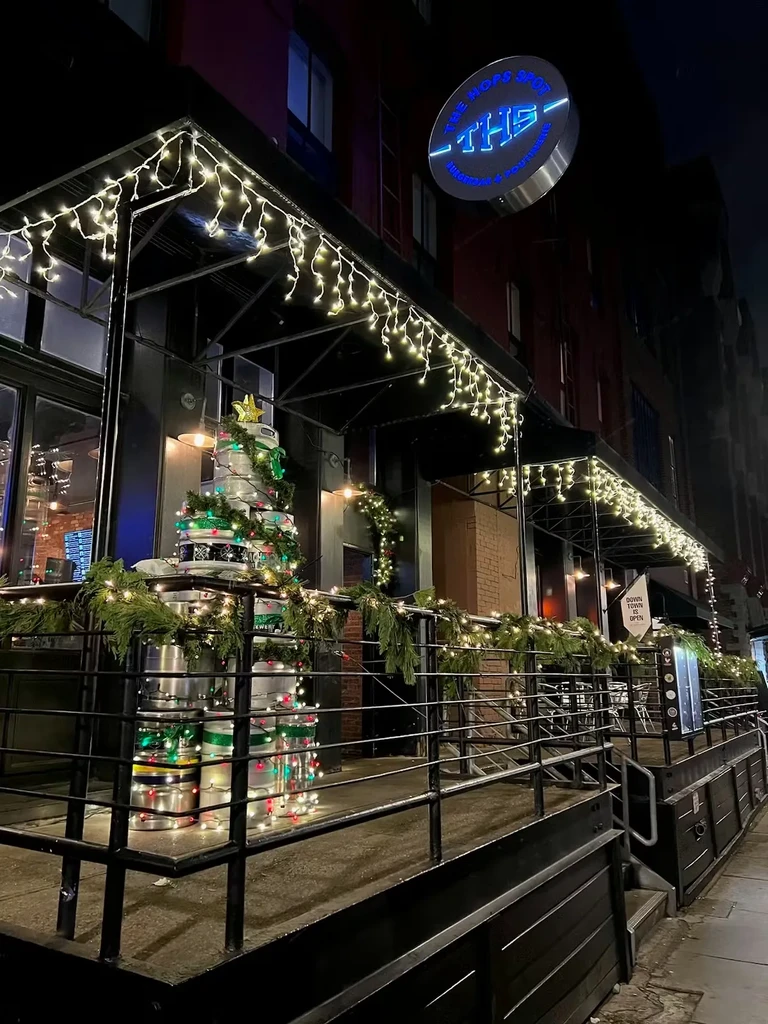 The Hops Spot exterior at night, decorated for holidays with a keg Christmas tree.