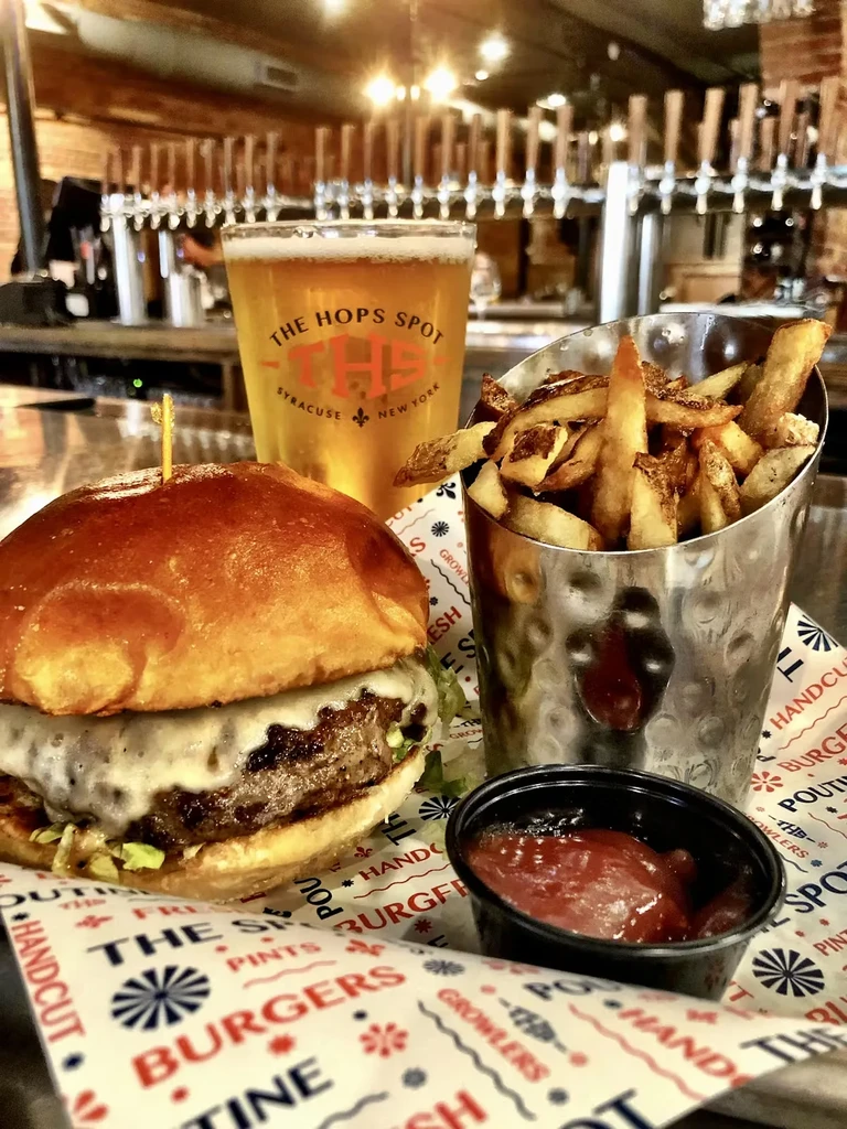 Cheeseburger, fries, ketchup, and "The Hops Spot" beer at a bar.
